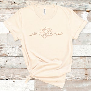 May include: A beige t-shirt with a brown line drawing of a flower and the words "inhale" and "exhale" on the front.