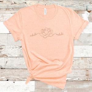 May include: A peach-colored t-shirt with a line drawing of a flower and the words "inhale" and "exhale" on the front.