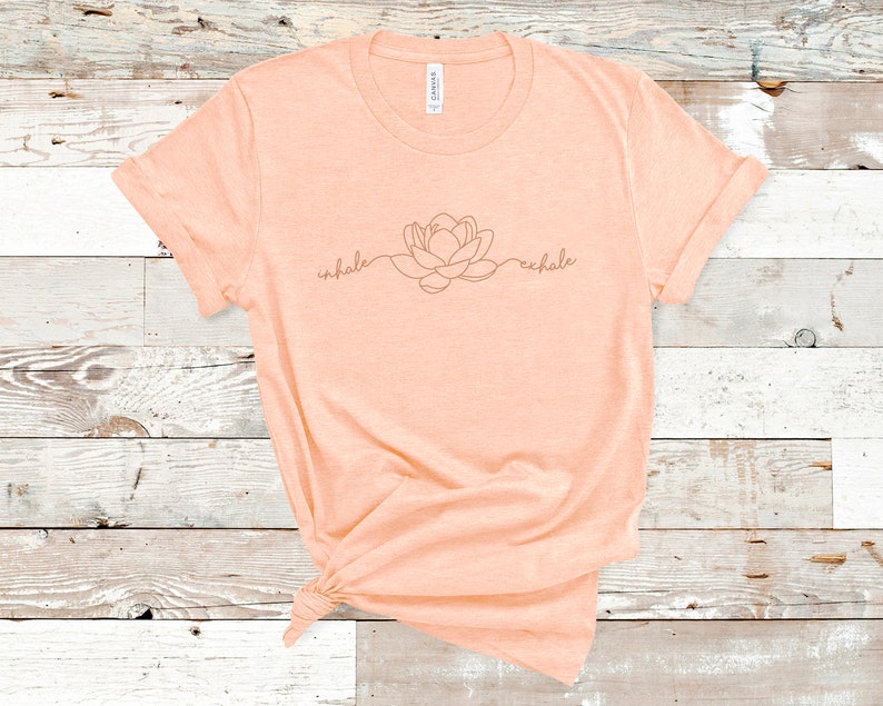 May include: A peach-colored t-shirt with a line drawing of a flower and the words "inhale" and "exhale" on the front.