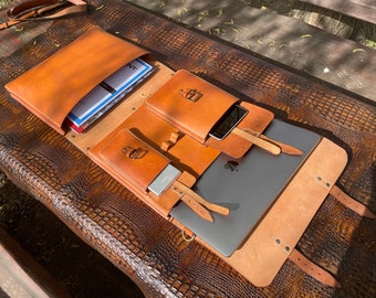 May include: A brown leather laptop bag with multiple pockets and straps. The bag is open and a laptop, notebook, and phone are visible inside.