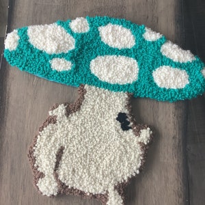 May include: A hand-crafted mushroom-shaped rug with a teal green top and white spots. The bottom of the rug is a light brown color.
