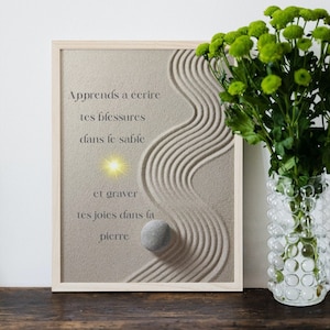 Peut inclure: Une impression encadrée avec une citation en français sur l'écriture de ses chagrins dans le sable et la gravure de ses joies dans la pierre. L'impression présente un design de jardin zen avec une pierre et une lumière qui brille sur le sable.