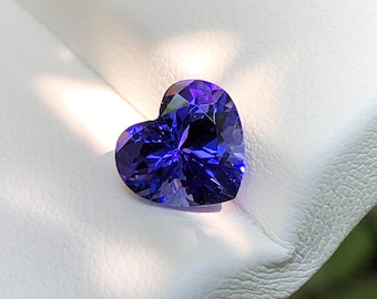 Può includere: Una gemma a forma di cuore di un colore viola-blu profondo e vibrante, con una superficie sfaccettata che riflette la luce. La pietra presenta una qualità trasparente con tagli geometrici netti che creano un aspetto brillante e luminoso.