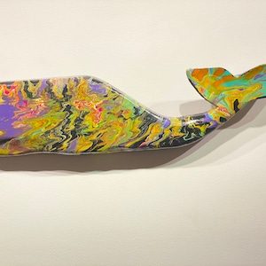 May include: A wooden whale sculpture painted with colorful abstract swirls of yellow, green, purple, orange, and black paint.