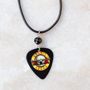May include: Black leather cord necklace with a black bead and a black guitar pick pendant featuring the Guns N' Roses logo.