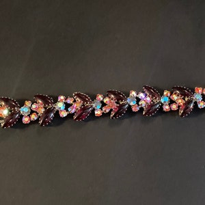 May include: A vintage bracelet with a silver tone metal base and a design of alternating dark purple and iridescent pink leaves with clear rhinestones.