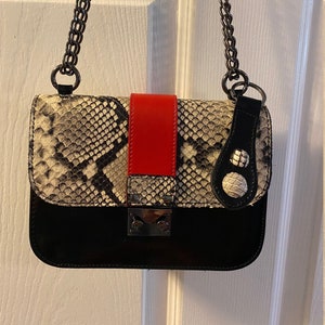 May include: A black and white snakeskin crossbody bag with a red leather accent and a silver chain strap.
