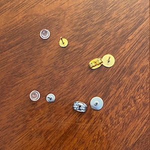 May include: Assortment of earring backs in gold and silver tones. The backs include a variety of styles, such as butterfly, push-back, and screw-back.