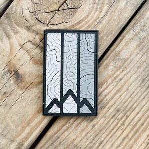 May include: A black and white topographic map patch with three mountain peaks at the bottom. The patch is rectangular and has a black border.