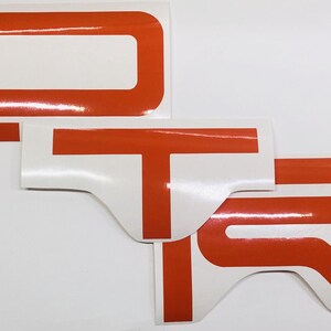 May include: Three white vinyl decals with orange lettering spelling out the word "DTR".