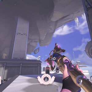 May include: A first-person view of a video game, showing a player holding a gold and purple weapon with a pink and white design. The player is standing on a snowy platform with a large, gray rock formation in the background.