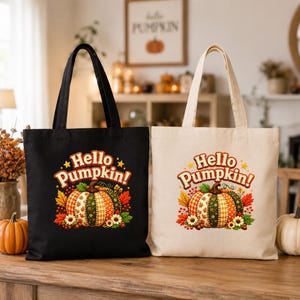 Op de afbeelding: Twee tote bags, een zwarte en een beige, elk met een afbeelding van een patchwork pompoen omringd door herfstbladeren en bloemen. De tekst "Hello Pumpkin!" is in een gestileerd lettertype boven de pompoen op beide tassen gedrukt.