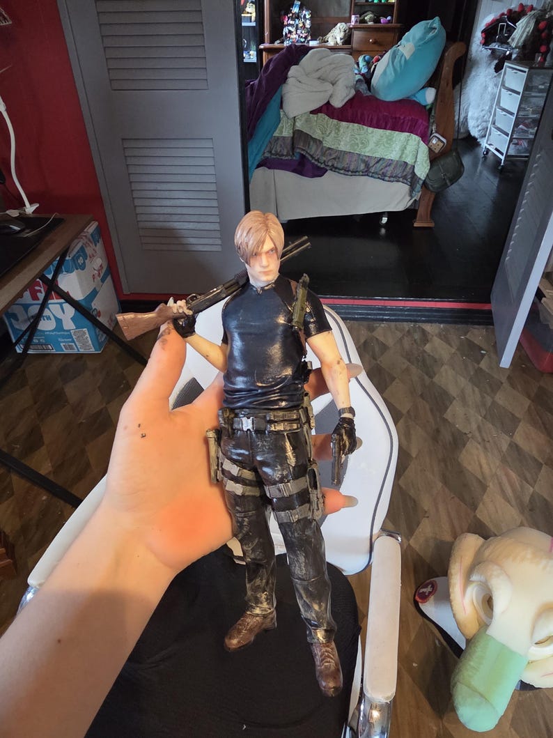 K&ouml;nnte beinhalten: Detaillierte Actionfigur eines m&auml;nnlichen Charakters, der eine Schrotflinte und eine Handfeuerwaffe h&auml;lt. Die Figur tr&auml;gt ein schwarzes Hemd, taktische Hosen und braune Stiefel. Die Figur ist etwa 30 cm gro&szlig;.