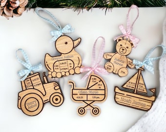 May include: Five wooden ornaments with blue and pink ribbons. Each ornament features a different design, including a tractor, a duck, a teddy bear, a stroller, and a sailboat. Each ornament includes a name, birth date, weight, and length.