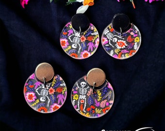 May include: A pair of colorful skeleton earrings with a floral pattern. The earrings are made of clear acrylic and have a black and gold metal backing. The earrings are a fun and festive way to add a touch of personality to any outfit.
