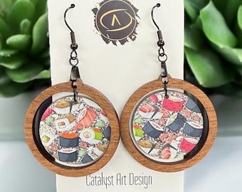 May include: A pair of wooden earrings with a round, clear resin insert featuring a colorful sushi design. The earrings have black metal hooks.