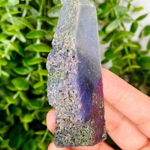 May include: A purple and green agate crystal point with a rough, textured surface. The crystal is a natural formation with a unique colour pattern.