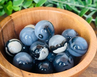May include: A wooden bowl filled with blue agate spheres. The spheres have white and black banding.