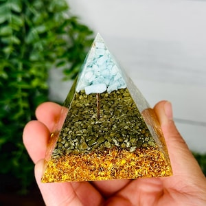May include: A clear pyramid with three layers of crystals. The top layer is light blue aquamarine, the middle layer is dark green pyrite, and the bottom layer is gold glitter.