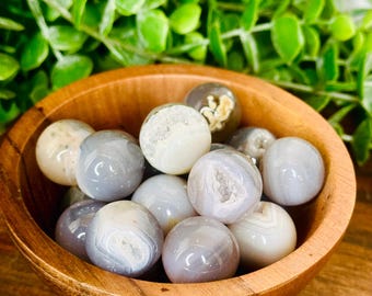 May include: A wooden bowl filled with gray and white agate spheres. The spheres are smooth and polished, with a variety of patterns and textures.