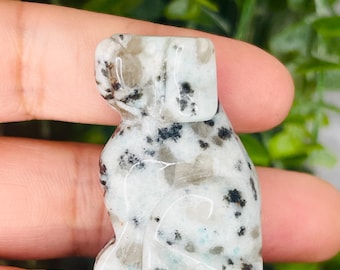 May include: A white and black speckled stone carved into the shape of a sitting dog. The dog is facing to the right and has a rounded head.