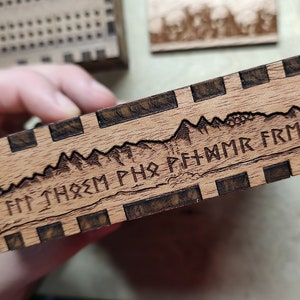 May include: A wooden box with a mountain range design and the inscription "FPT THREM PHO PFTHMMR FRM IRET" carved into the wood.