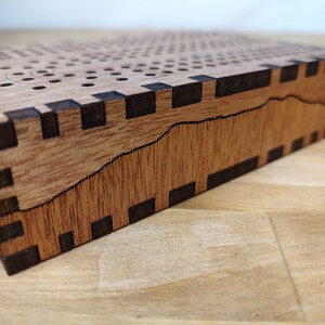 May include: A wooden game board with a black inlay design. The board is made of light wood and has a dark wood inlay around the edges.