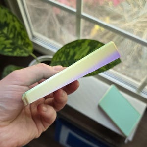 Peut inclure: Gros plan sur le bord d'un carnet jaune clair et violet. Le carnet est fait de papier texturé et présente un dégradé subtil du jaune au violet.