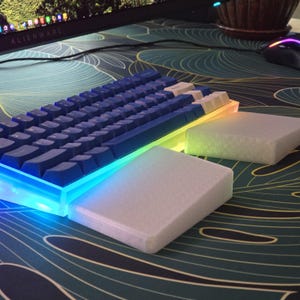 Könnte beinhalten: Eine blaue mechanische Tastatur mit weißen Tastenkappen und RGB-Beleuchtung. Die Tastatur steht auf zwei weißen Untersetzern.
