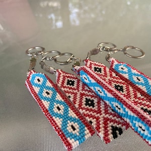 May include: Four beaded keychains with red, white, blue, and black geometric patterns. The keychains are attached to silver key rings.