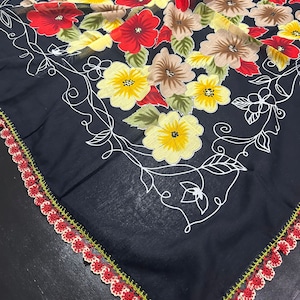 May include: A black square scarf with a floral pattern in shades of red, yellow, and brown. The scarf has a crocheted border in red, green, and white.