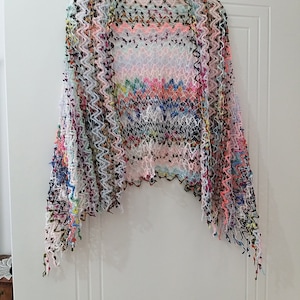 May include: A colorful crocheted shawl with a zig-zag pattern and fringe edges.