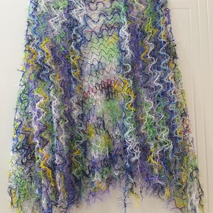 May include: A colorful crocheted shawl with a fringe border. The shawl is made with a variety of colors, including blue, green, yellow, and white.
