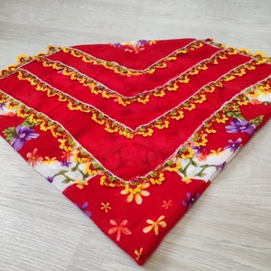 May include: Red and white fabric square with a floral pattern and yellow crocheted trim.