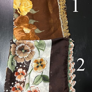 May include: Two brown floral patterned scarves with crocheted trim. The top scarf has a yellow and brown floral pattern. The bottom scarf has a white background with brown, orange, and green floral pattern.