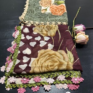 May include: Two floral patterned scarves with crocheted lace trim. The top scarf is green with orange roses and the bottom scarf is maroon with brown roses and white hearts. The scarves are numbered 1 and 2.