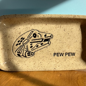 May include: A beige ceramic tray with a black and white illustration of a spaceship and the text "PEW PEW".