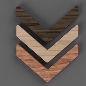 Könnte beinhalten: Drei hölzerne Wanddekorationen in Chevron-Form in verschiedenen Braun-, Beige- und Rotbrauntönen. Die Teile sind in einer gestapelten, nach unten zeigenden Pfeilformation vor einem grauen Hintergrund angeordnet.