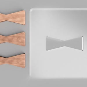 May include: Three wooden bow ties with a natural wood grain finish are displayed next to a white, rectangular surface with a bow tie shape. The bow ties are a light brown color and have a classic shape.