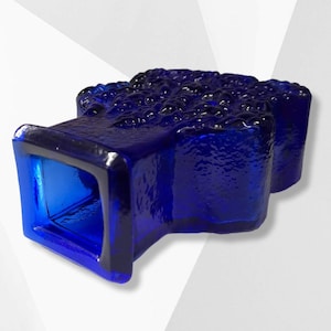 May include: A cobalt blue glass vase with a textured, bubbly surface. The vase has a rectangular opening and a unique, organic shape. The glass is transparent, allowing light to pass through, and the color is a deep, rich blue.