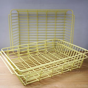 May include: Two rectangular wire baskets with a pale yellow finish. The baskets feature a grid-like construction with thin metal bars forming the base and sides, and each includes integrated handles on the shorter ends for easy lifting and transport.