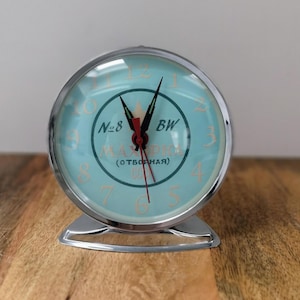 May include: A vintage silver alarm clock with a light blue face and black numbers. The clock face also has the text "N:8 BW MAЯKA (OTБOPHAЯ)".