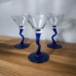 May include: Three blue-stemmed martini glasses with a clear glass bowl. The stems are twisted and the base of each glass is a solid blue color.