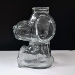 以下が含まれることがあります： 座っている犬の形をした透明なガラス製の貯金箱。貯金箱の上部にコインを入れるためのスロットがあります。