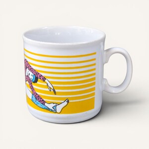 Puede incluir: Taza de cerámica blanca con un fondo a rayas amarillas y blancas. La taza presenta una colorida ilustración de una persona con un top rosa con estampado de leopardo y pantalones cortos azules. La taza tiene un asa curva.
