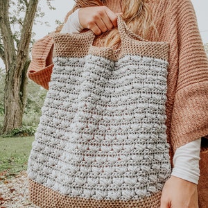 May include: A crocheted tote bag with a brown and gray color scheme. The bag has a textured design and is made with a thick yarn.