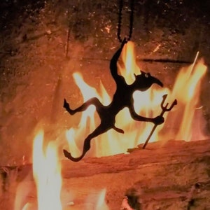 May include: A black metal silhouette of a devil holding a trident hangs in front of a fireplace with flames.