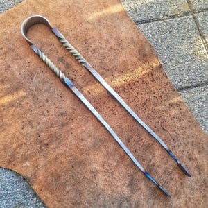Könnte beinhalten: Eine lange Zange aus Metall mit einem gedrehten Griff. Die Zange ist aus Stahl und hat eine blau-graue Oberfläche.