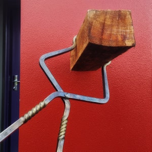 Könnte beinhalten: Ein Feuerwerkzeug aus Metall mit einem Holzgriff. Das Werkzeug ist sternförmig und hat einen langen, dünnen Griff. Das Werkzeug liegt an einer roten Wand.