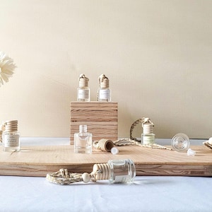 May include: Several small, clear glass bottles with wooden tops and labels, some with text. The bottles are arranged on a wooden surface, with a wooden block in the background. The bottles are connected to a rope.